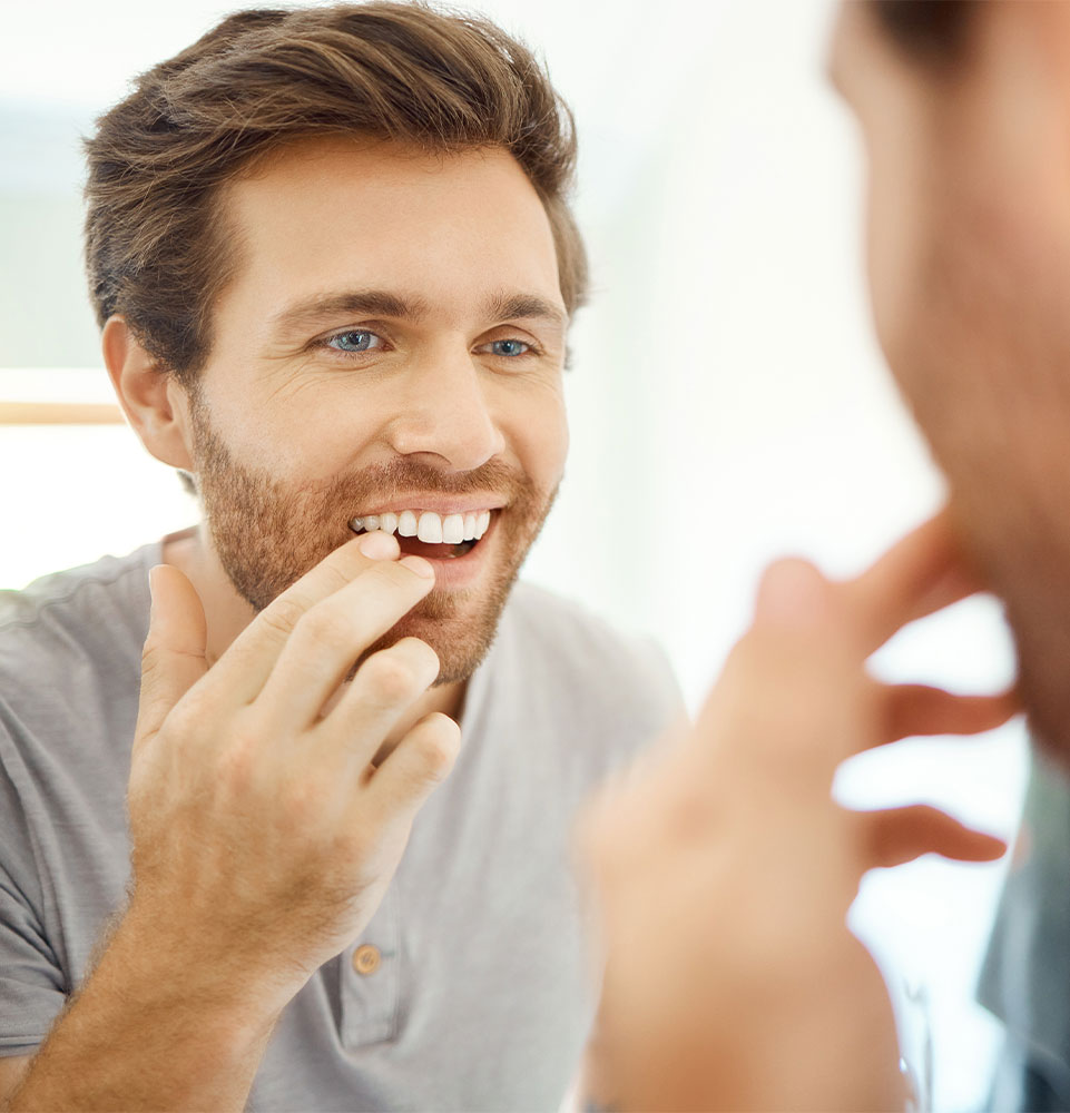 young male looking in the mirror checking on their tooth